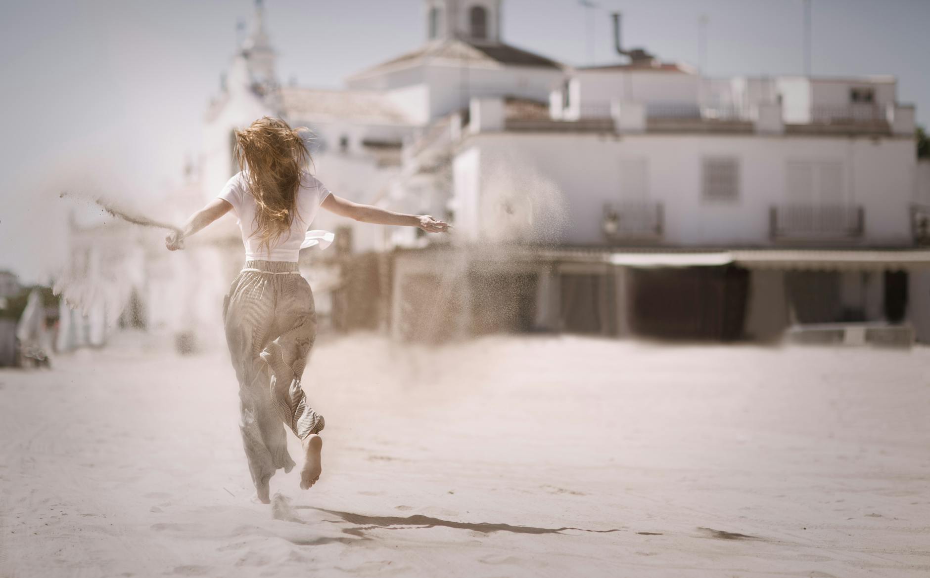 woman running on sand near white concrete building
